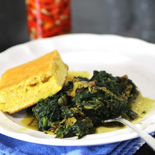 homemade mustard greens with cornbread and hot pepper vinegar sauce on a white plate