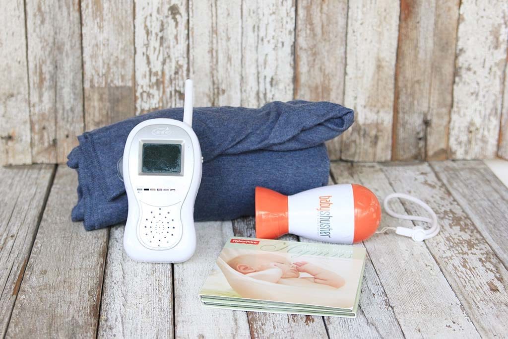 Newborn Baby Essentials Checklist for a first time mom: video baby monitor, fisher price babies first hymns cd, baby shusher, and a moby wrap on a white chippy wood backdrop