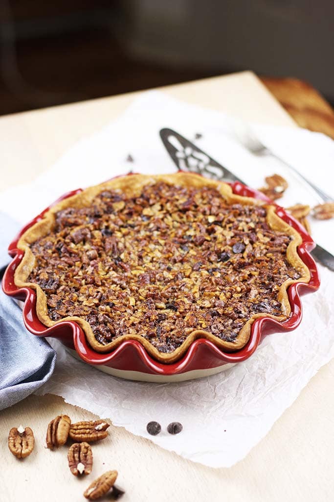 a whole chocolate chip pecan pie in a red, ruffled pie dish