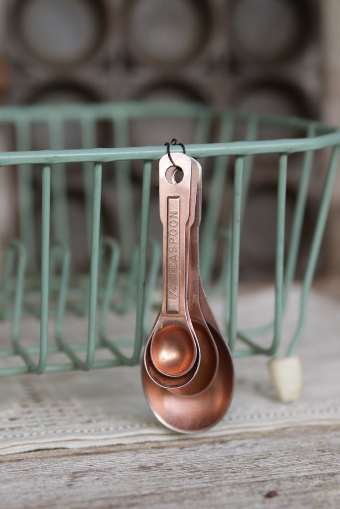 a set of copper colored measuring spoons hanging on a vintage green dish drain