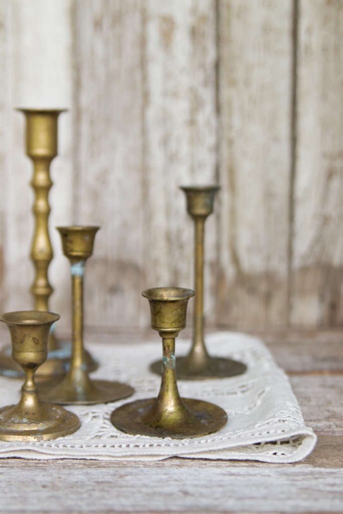 vintage brass candlesticks on a white linen table runner sitting on chippy white painted boards