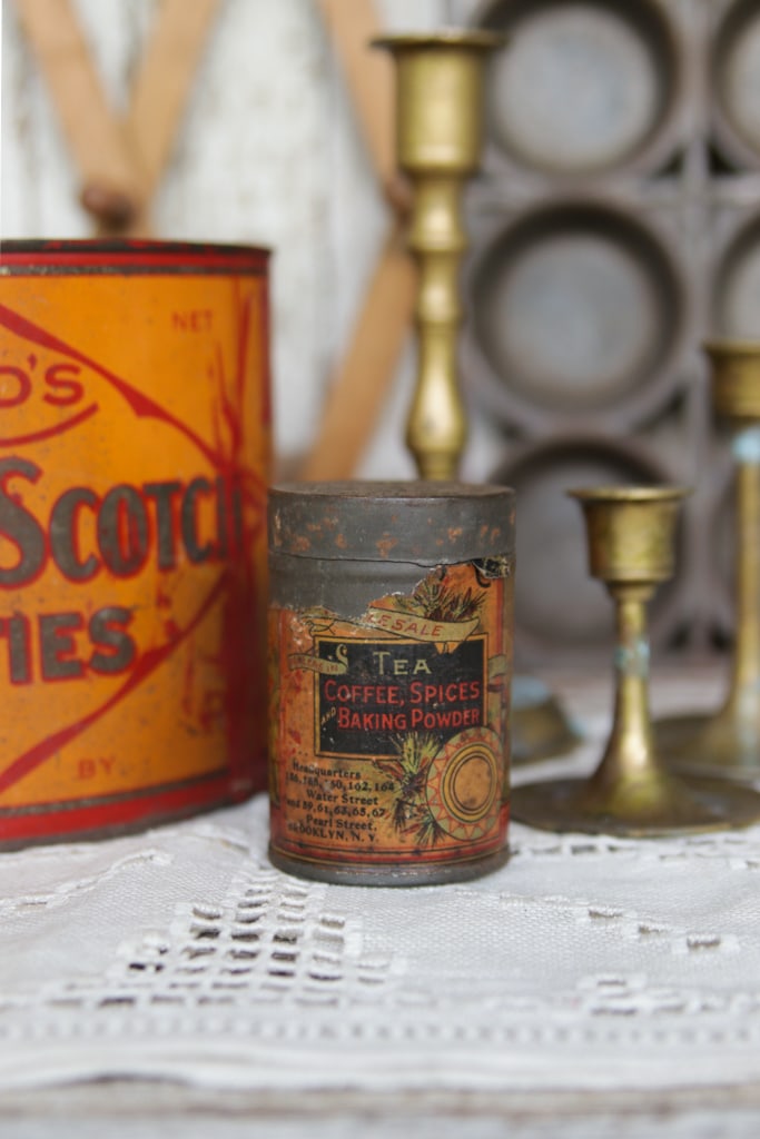 a small orange vintage tea tin next to a reed's butter scotch patties tin and three antique brass candlesticks
