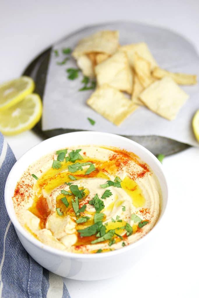 chickpea hummus in a white bowl with pita chips and lemon