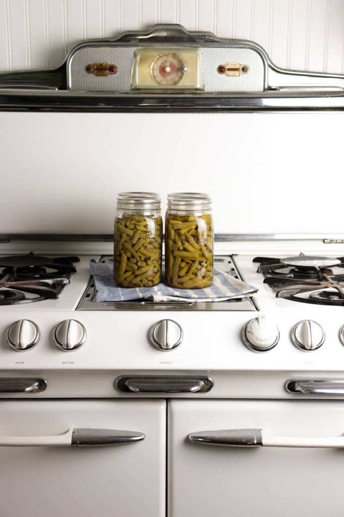 pressure canned homegrown green beans sitting on a vintage O'Keefe and merritt gas stove with a blue and cream striped tea towels