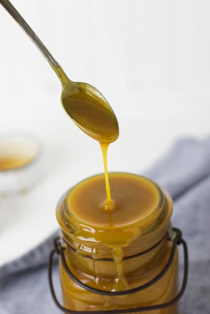 healthy honey mustard dressing dripping off of a spoon into a vintage ball jar