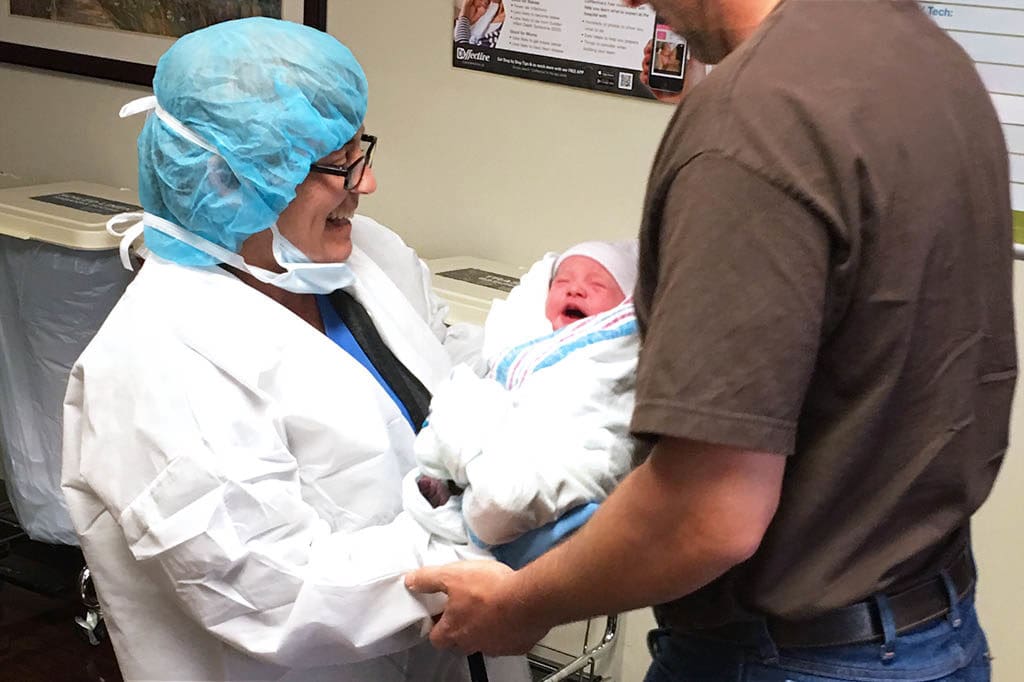 Nurse handing newborn baby to father