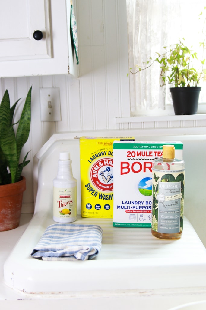 liquid castille soap, borax, washing soda, and thieves cleaner on a white double drainboard sink