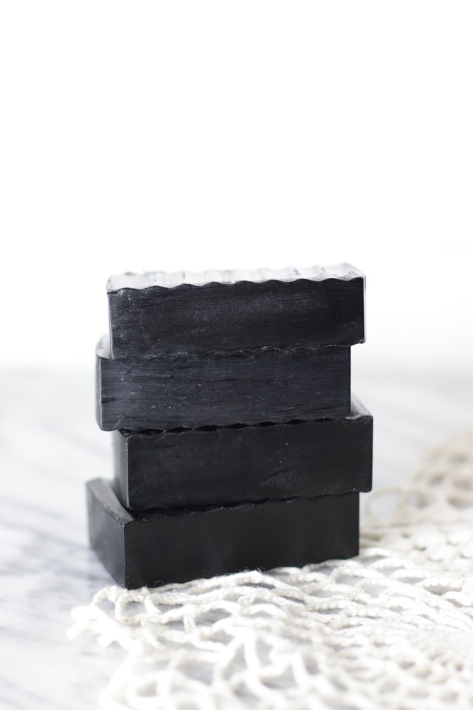 4 bars of black charcoal soap on a white doily and a white and gray marble countertop