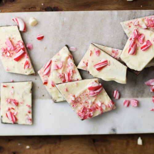 homemade peppermint bark on a marble cutting board with peppermint pieces scattered around