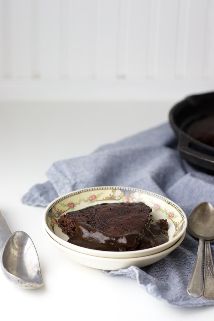 dairy free chocolate cobbler in a small antique bowl on a white counter with a blue tea towel