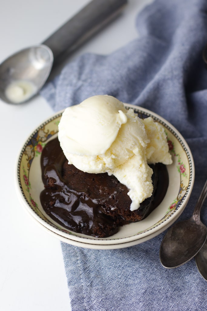 hot fudge pudding cake with ice cream in a vintage china bowl on a white counter with a blue tea towel 