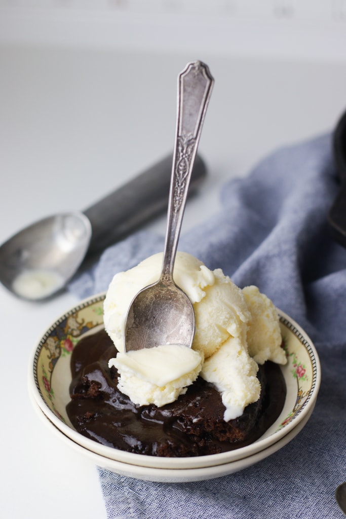 a vintage silver spoon scooping a bite of ice cream and chocolate hot fudge cake out of an antique china bowl
